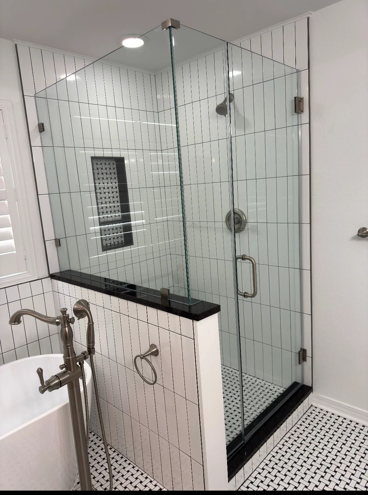 Bathroom with a freestanding tub, frameless glass shower, white vertical tile, black fixtures, and patterned floor tile.