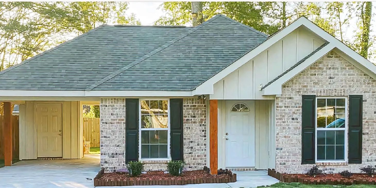Customer-supplied front view of a light brick home with white siding and a covered carport.