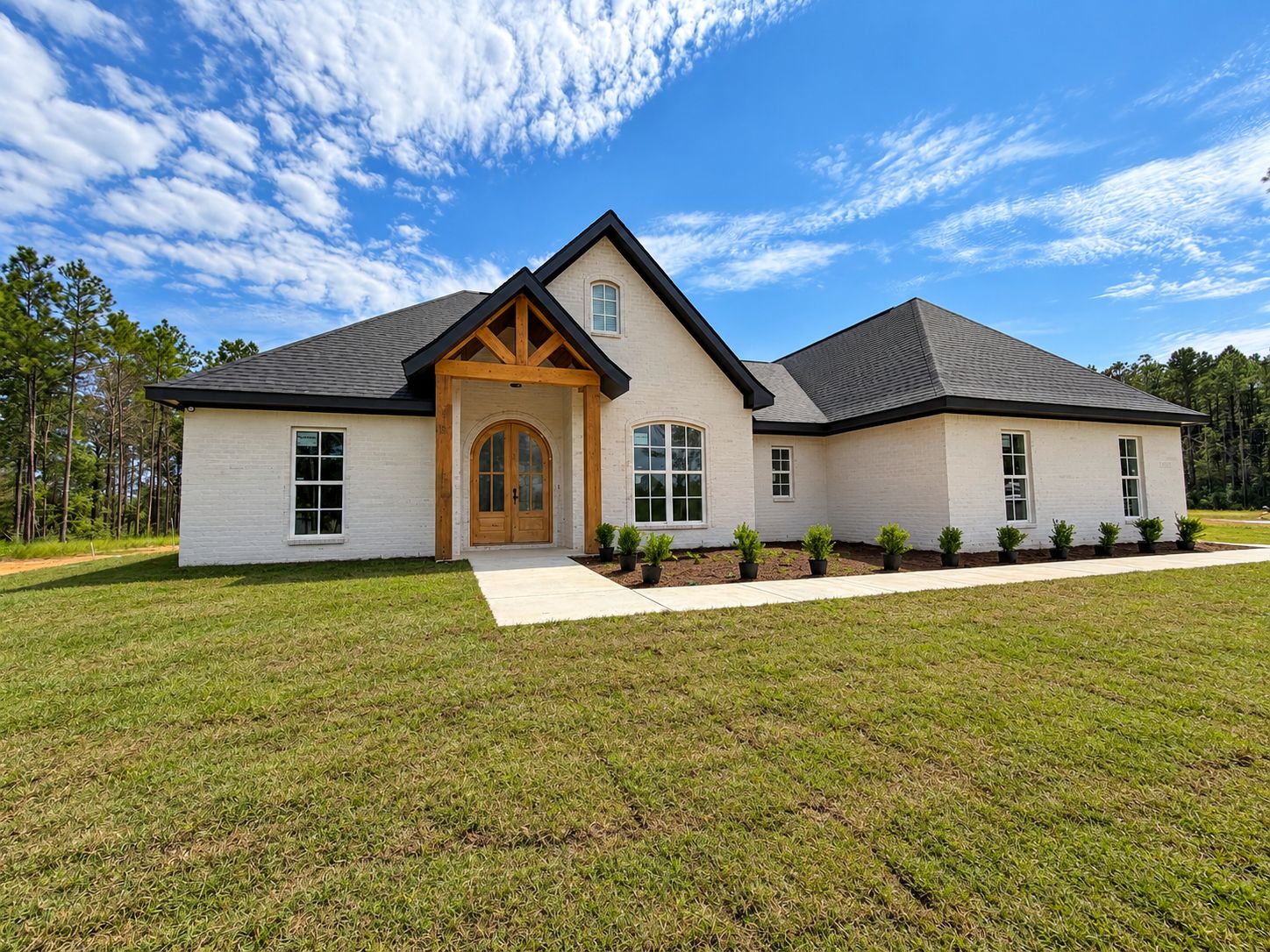 Front exterior of a completed white home with a dark roof and timber entry detail.