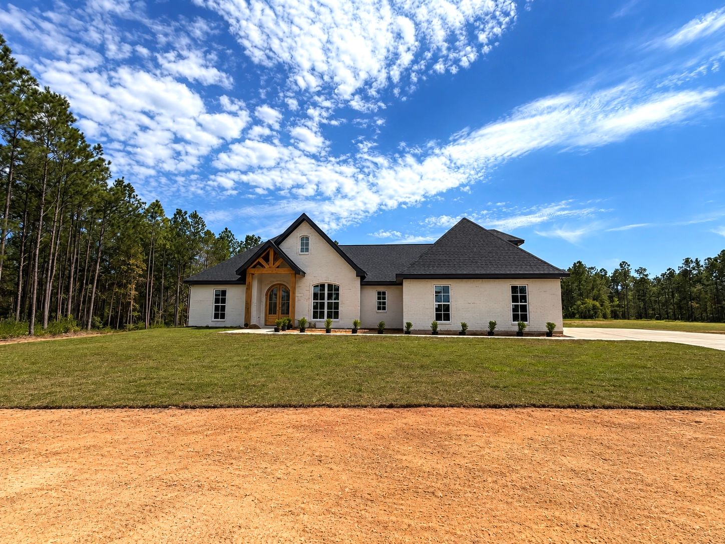 Wide front view of the completed white home beside a wooded lot.
