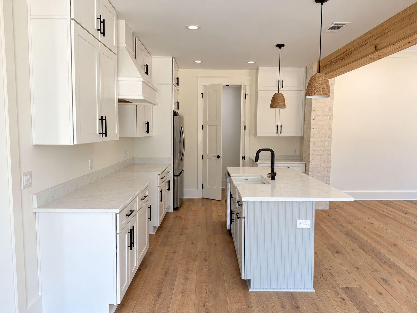White kitchen with an island, pendant lights, and an exposed timber beam.
