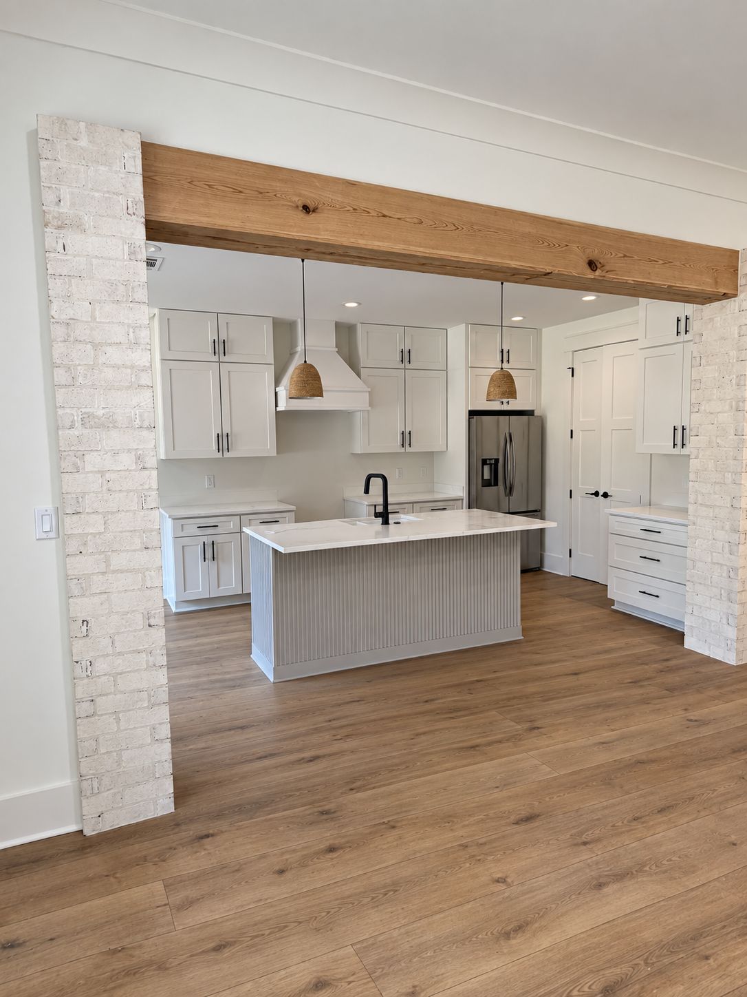 View through a brick-trimmed opening into the white kitchen and island.