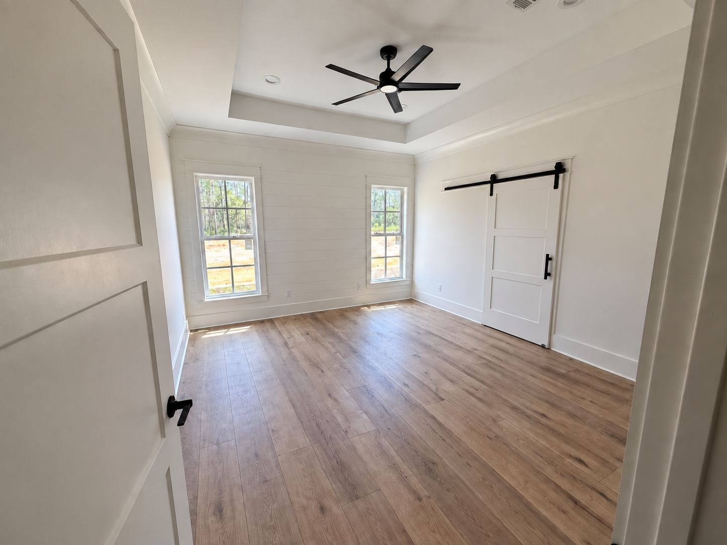 Room with a tray ceiling, black ceiling fan, sliding barn door, and wood-look flooring.