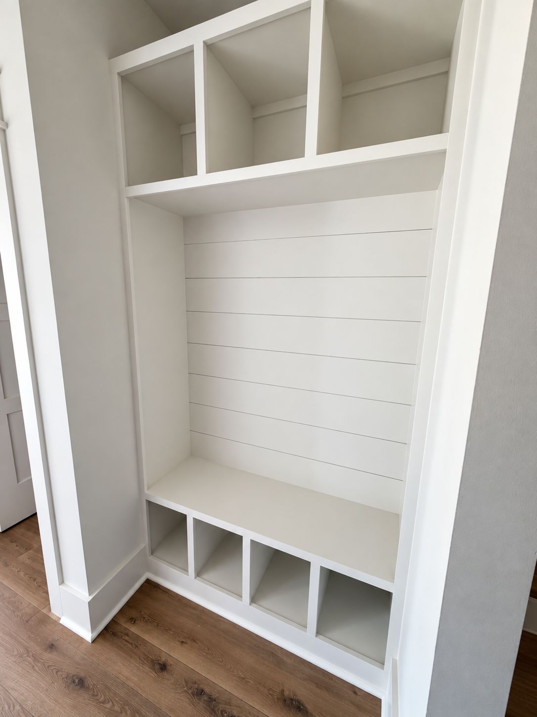 Built-in white mudroom bench with upper cubbies, hooks, and shoe storage.