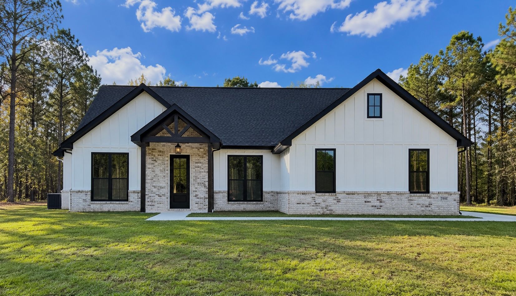 Front exterior of a completed white home with a dark roof, brick base, and covered entry.