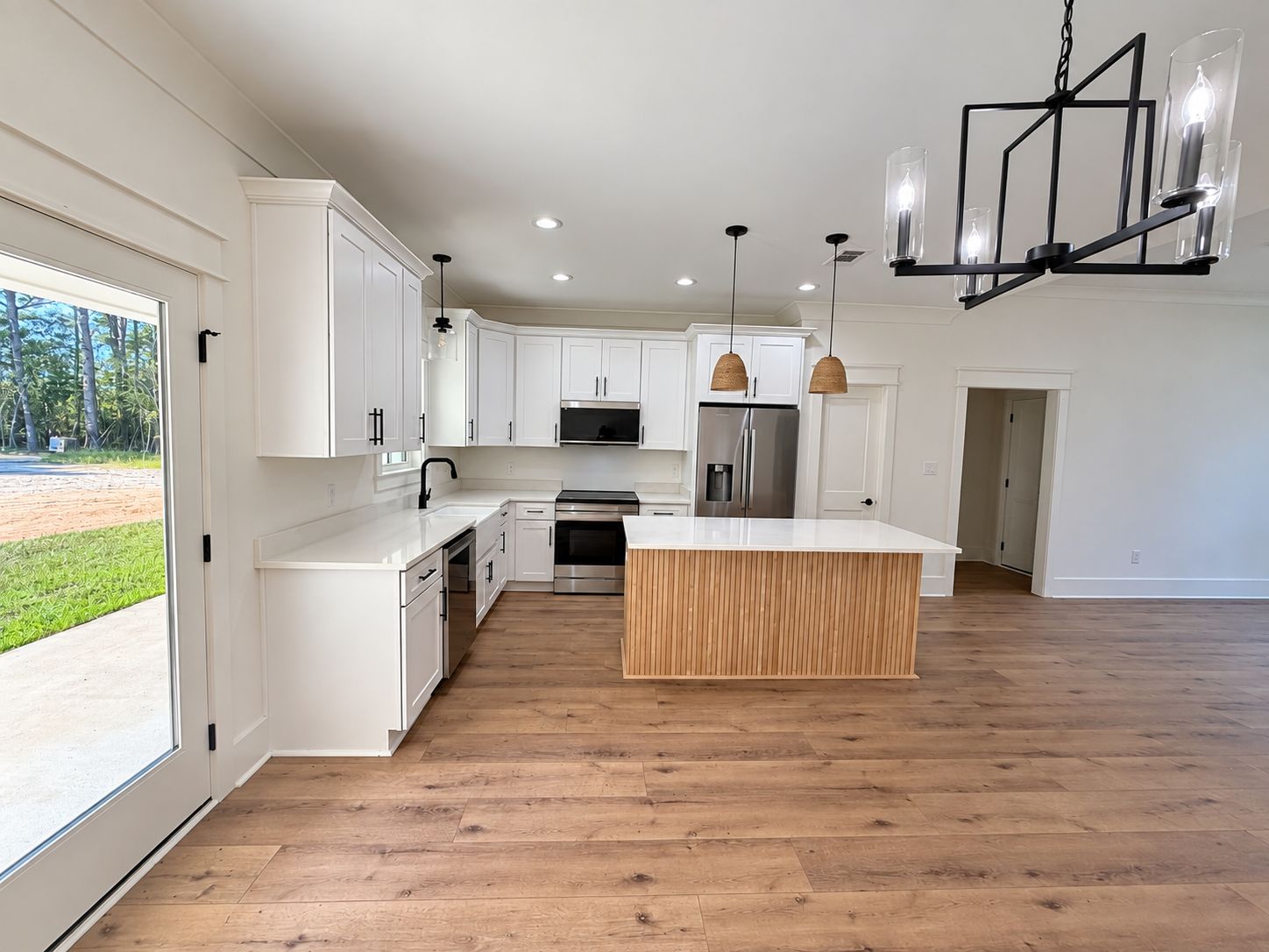 Open kitchen and living area with white cabinetry, a wood island, and black light fixtures.