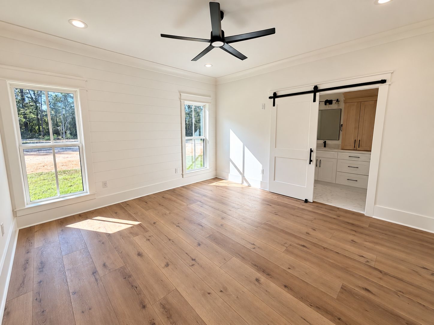 Bright room with three windows, a black ceiling fan, and a sliding barn door.