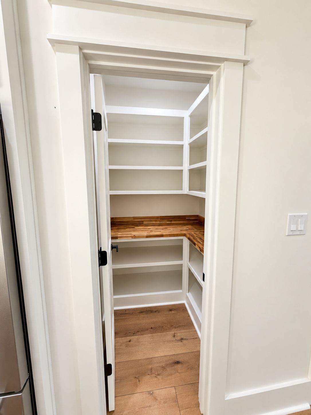 Compact pantry with white shelving and a wood counter surface.
