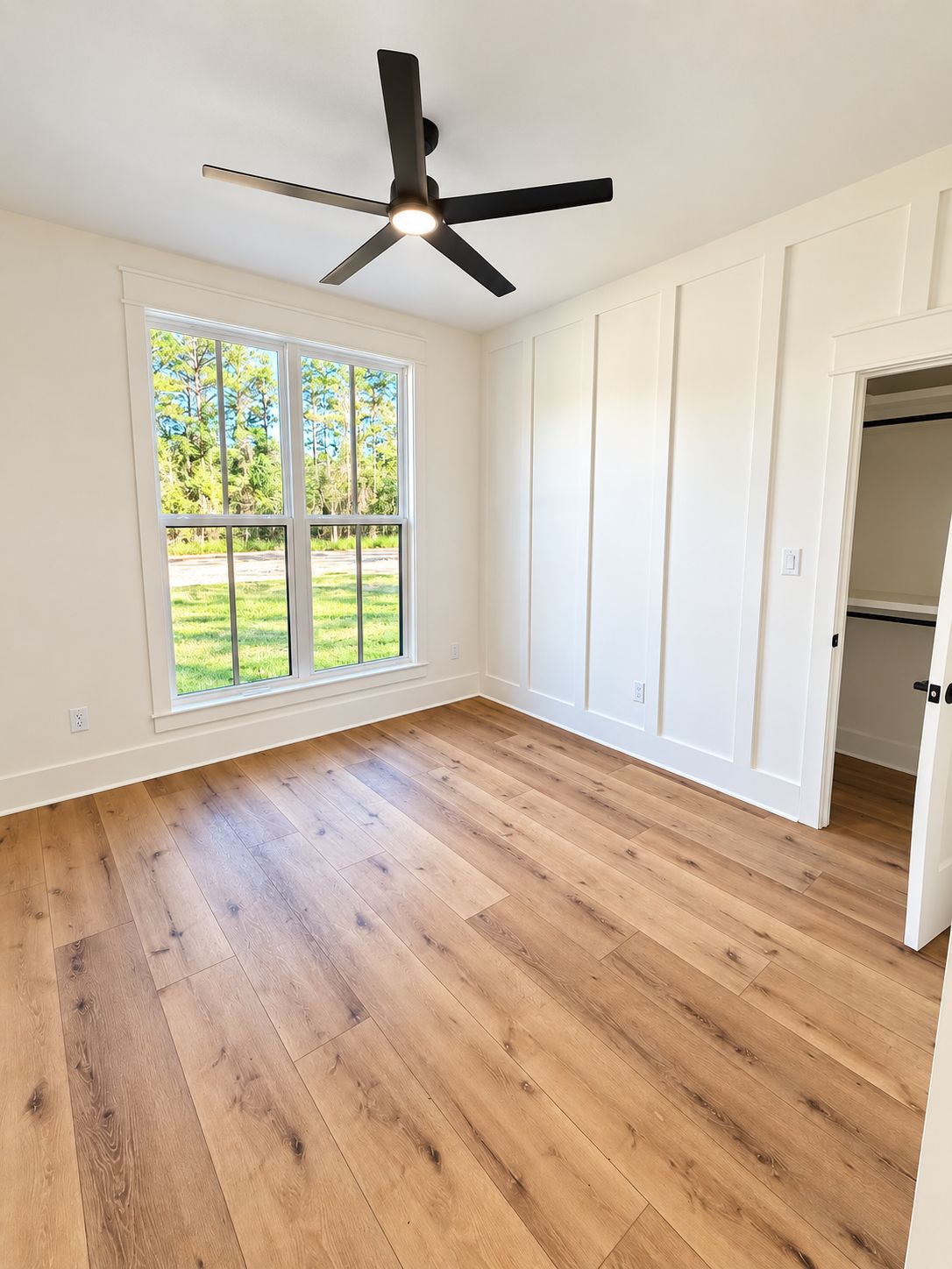 Room with a large window, black ceiling fan, and white built-in wall cabinets.