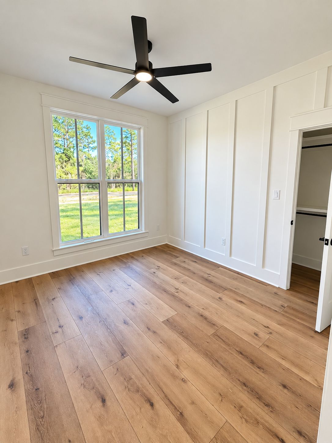 Room with a wide window, white built-in cabinets, and wood-look flooring.
