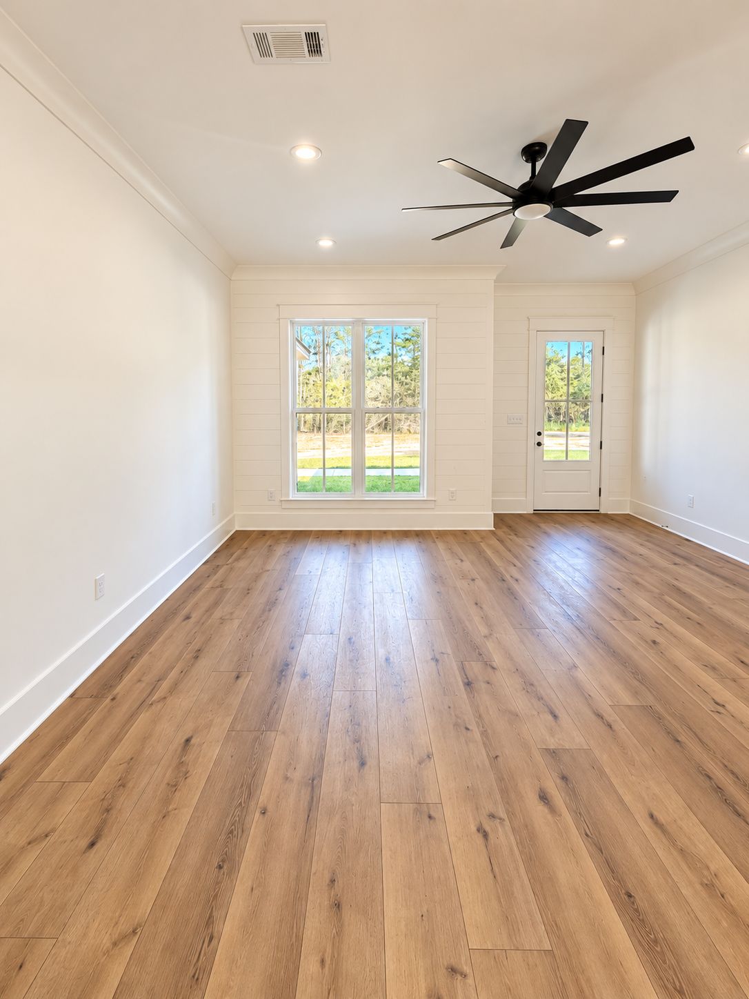 Room with two tall windows, a black ceiling fan, and wood-look flooring.