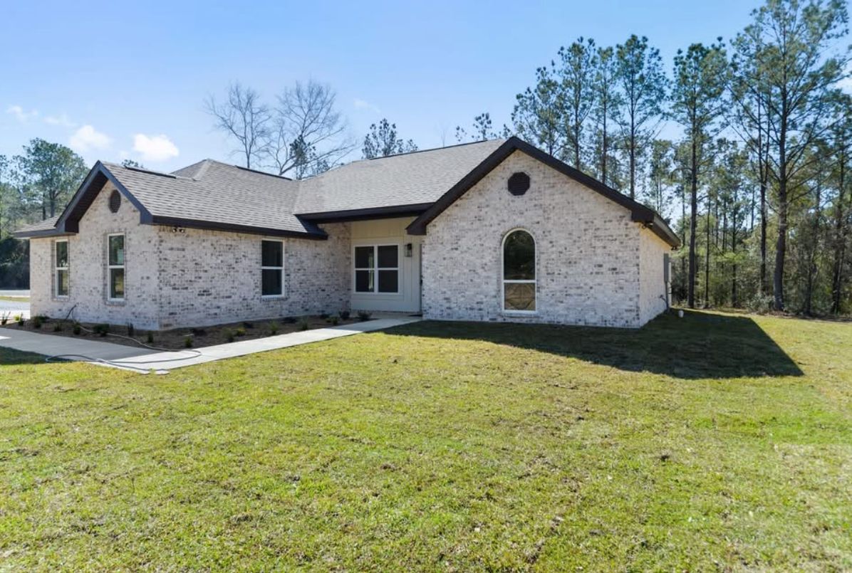 Angled front exterior of a completed light brick home with dark roof trim.