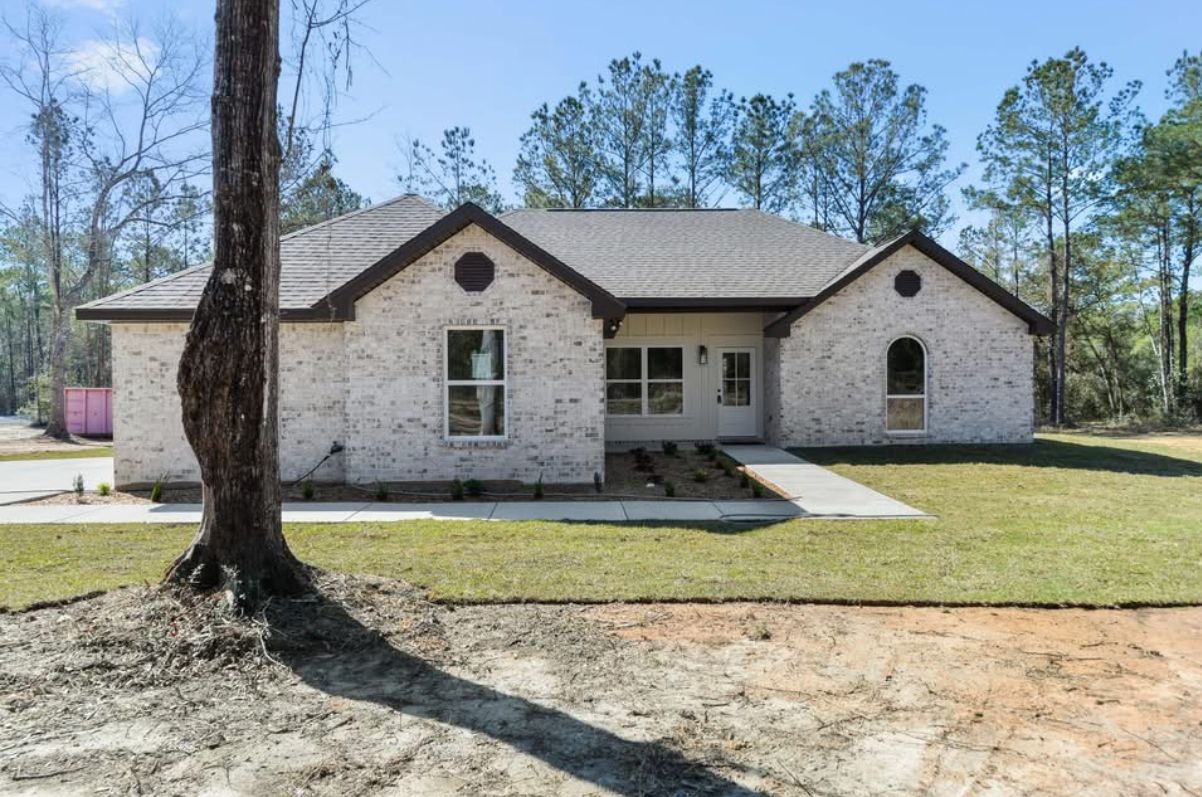 Front exterior of the light brick home with a mature tree in the foreground.