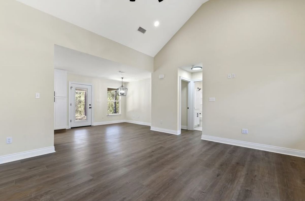 Open living and dining area with a vaulted ceiling and wood-look flooring.