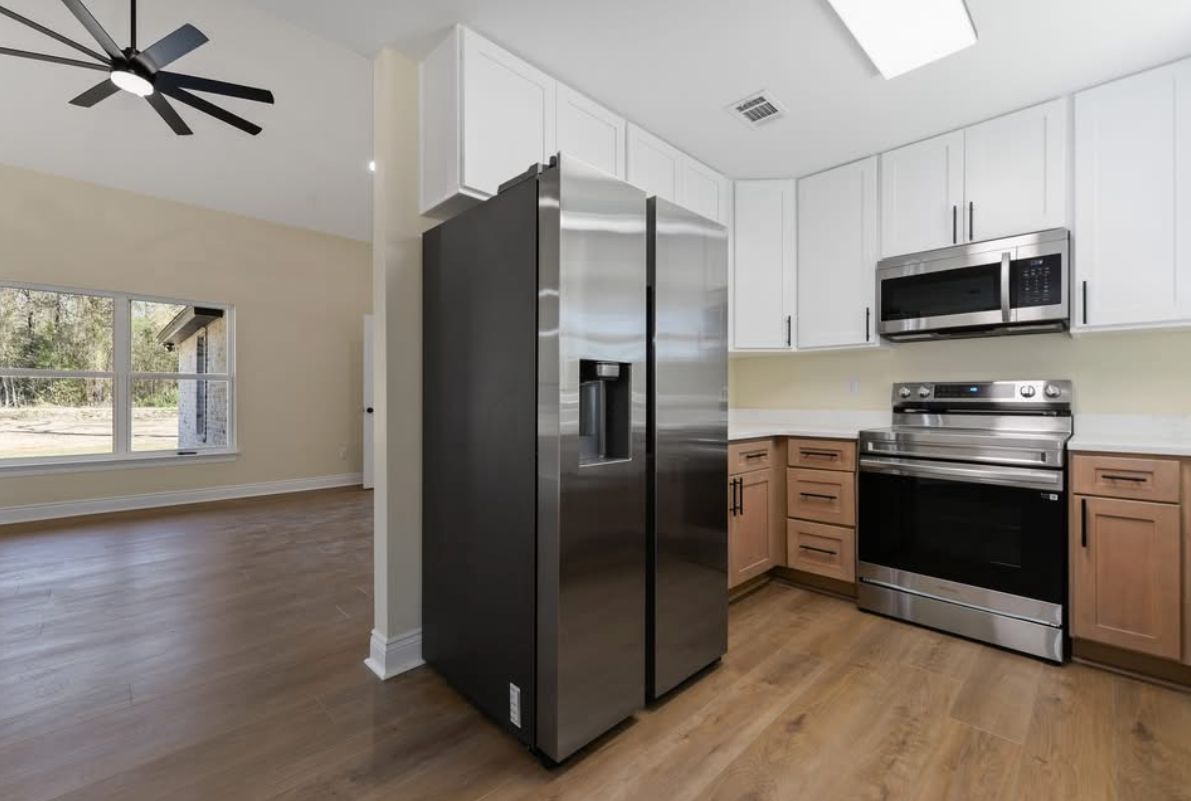 Wide kitchen view with white and wood cabinetry and stainless steel appliances.