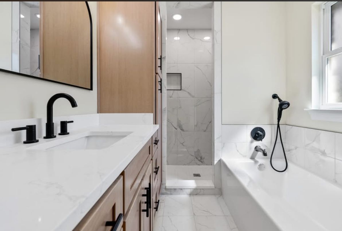 Bathroom with a white vanity, black fixtures, and a marble-patterned tub surround.