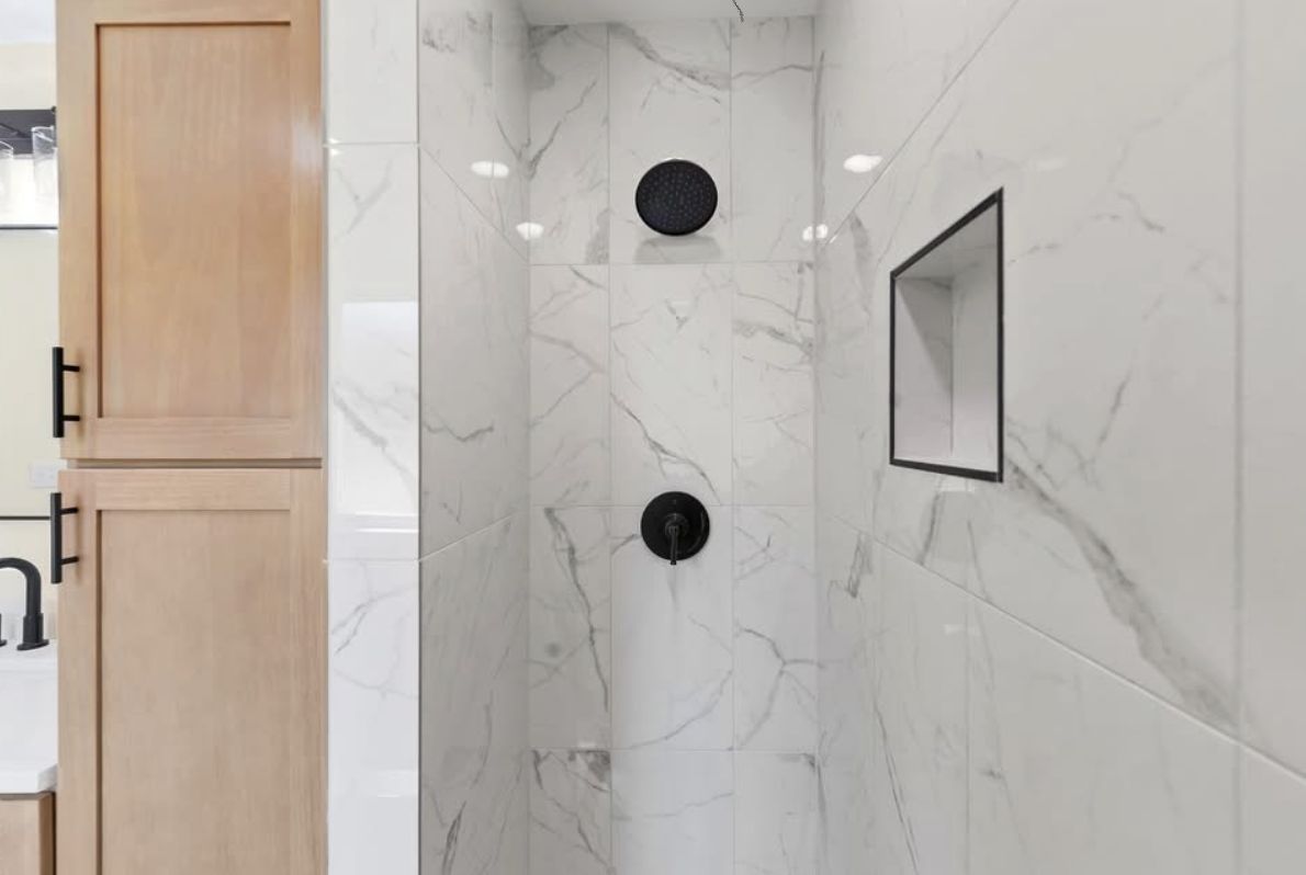 Marble-patterned shower with black fixtures and a recessed niche.