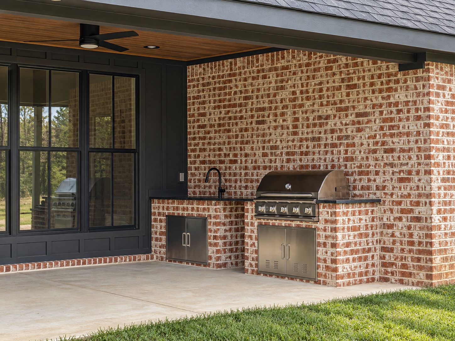 Covered brick patio with black-framed doors and windows, a ceiling fan, and a built-in grill.