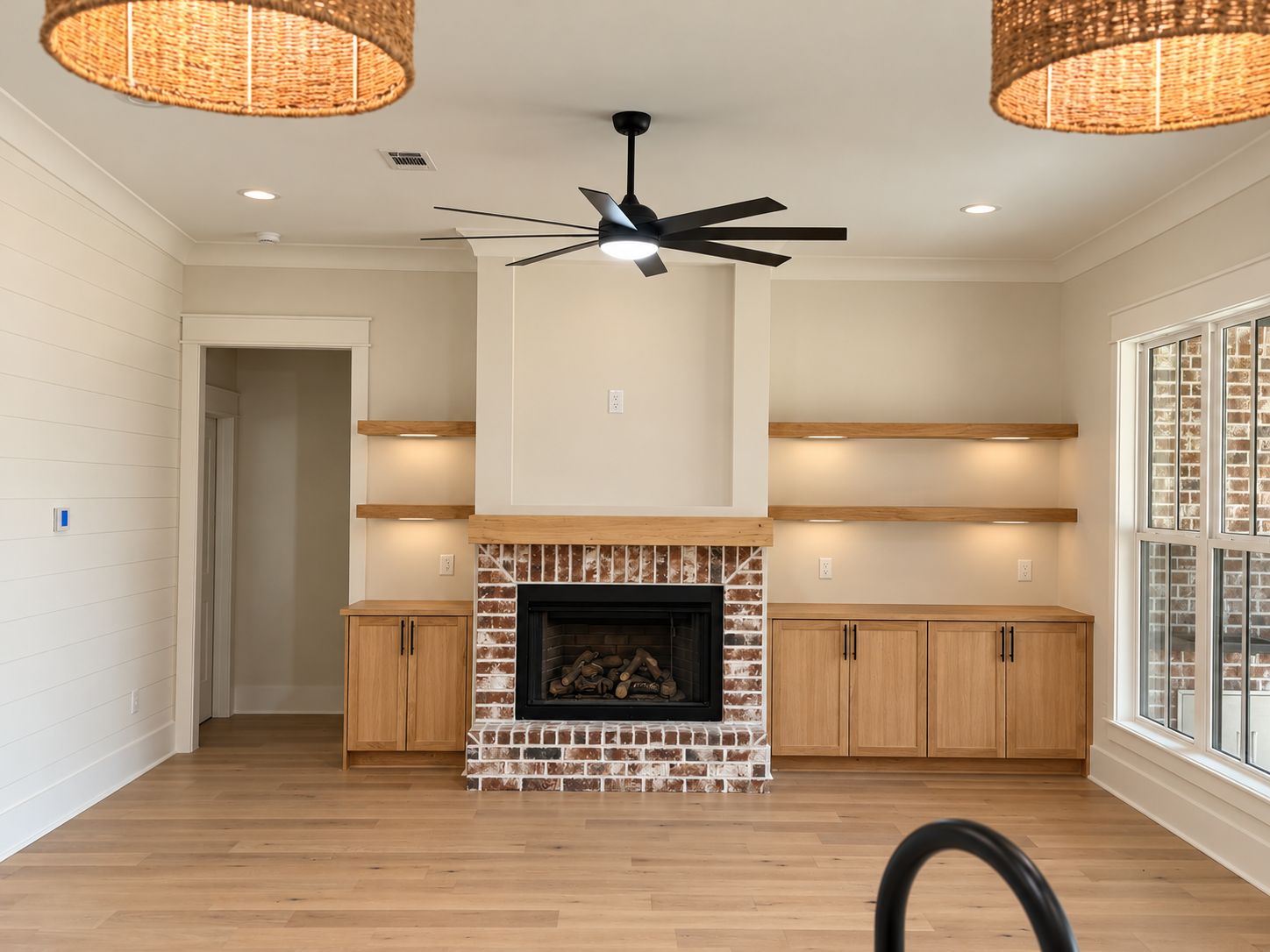 Living room with wood flooring, a brick fireplace, wood built-in cabinets, and woven pendant lights.
