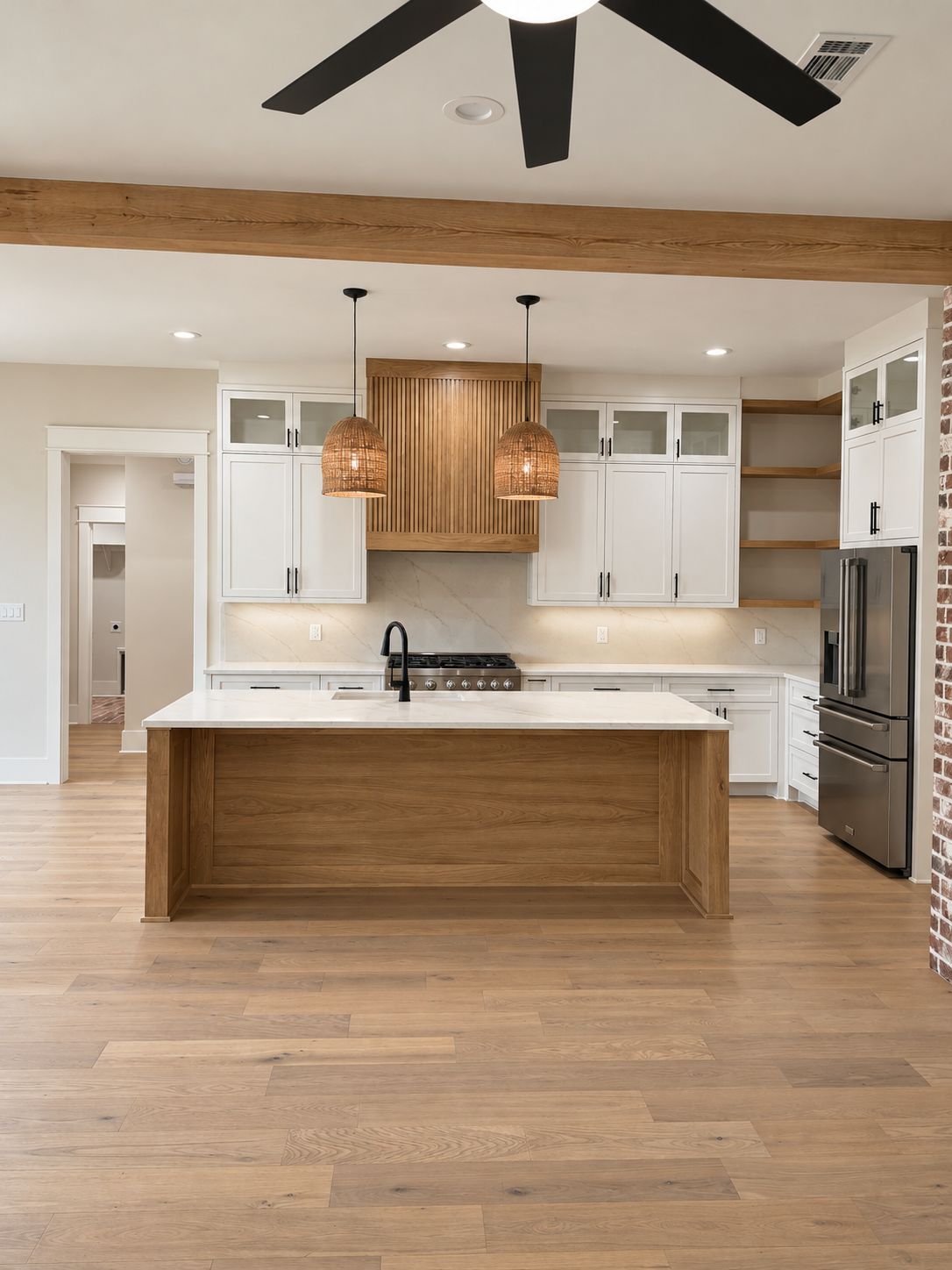 Kitchen with white cabinetry, a wood island, exposed ceiling beams, and black pendant lights.