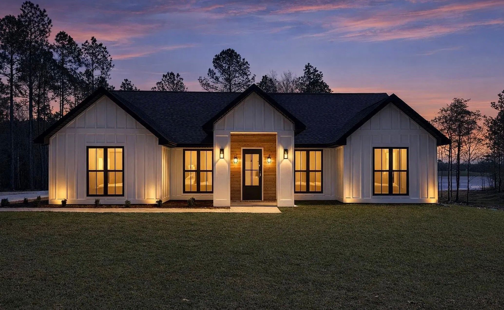 Front exterior of a completed white home with black trim and warm exterior lighting at dusk.