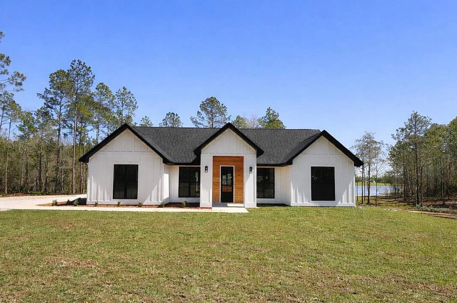 Front exterior of the white home with black trim, a wood entry door, and lawn.