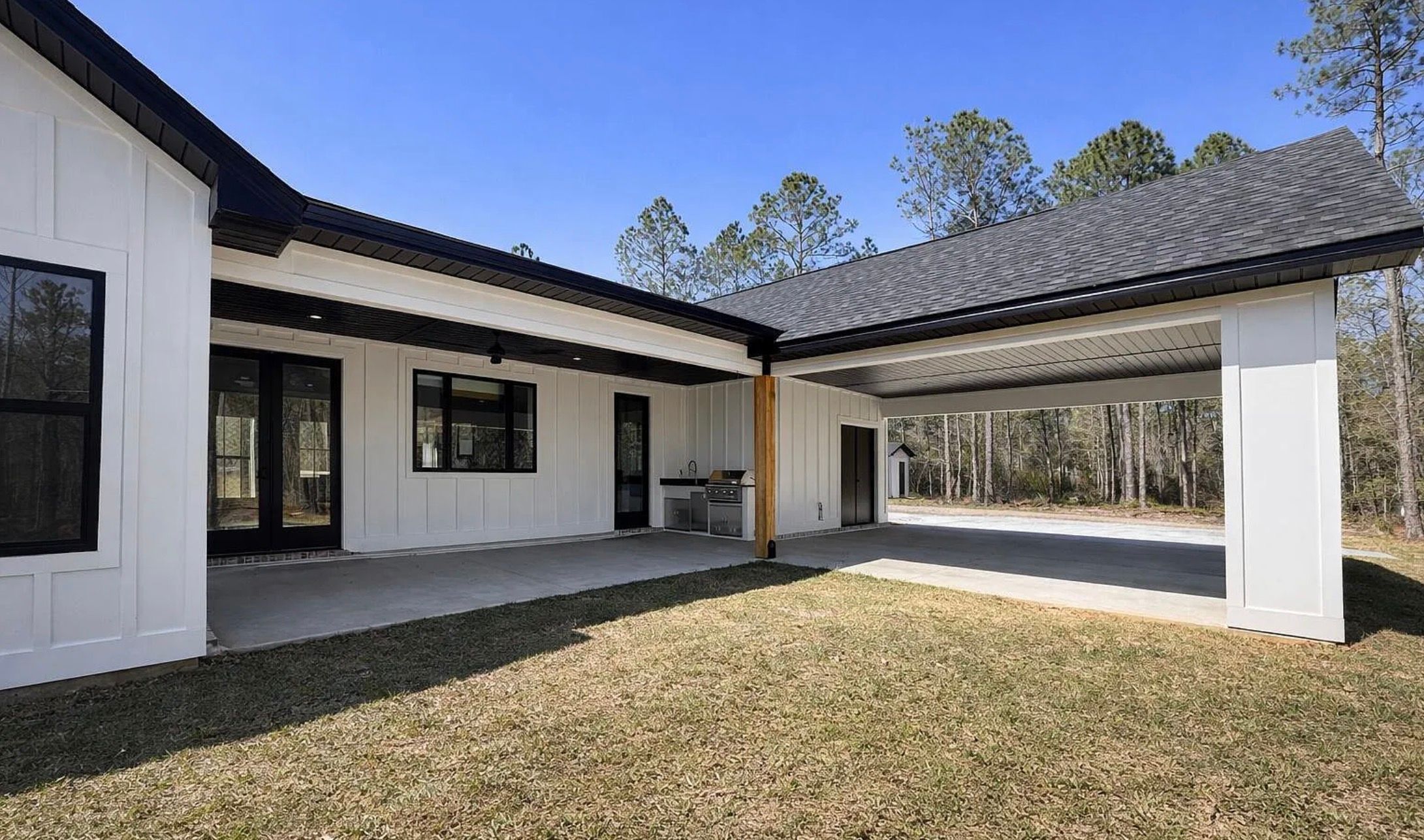 Rear exterior with white siding, black-framed windows, and a covered patio.