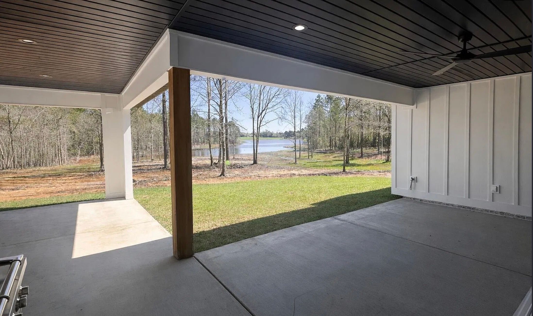 Covered patio with a dark ceiling, white columns, and a view of the yard and water.