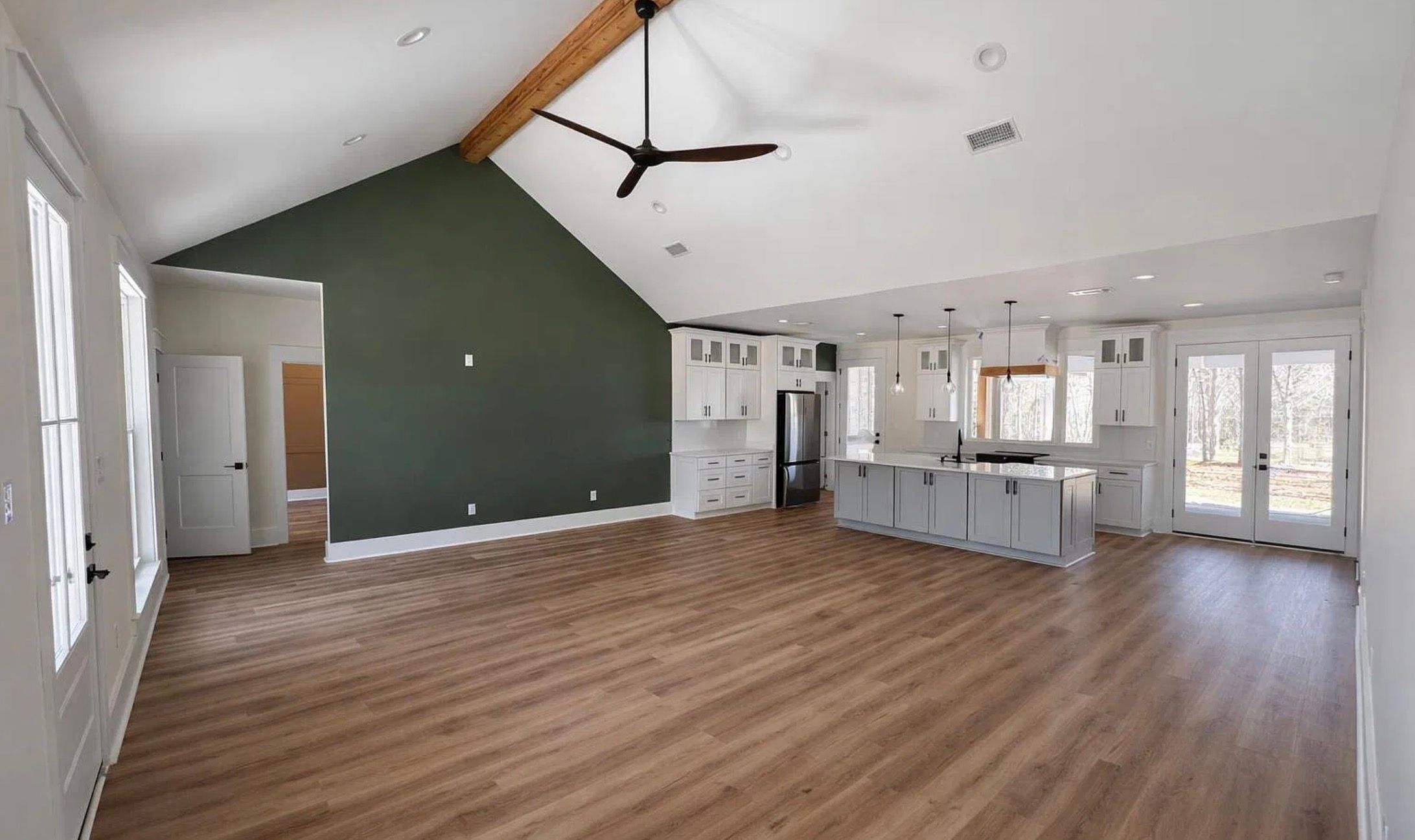 Open living and kitchen area with a vaulted ceiling, exposed wood beam, green accent wall, and white cabinetry.