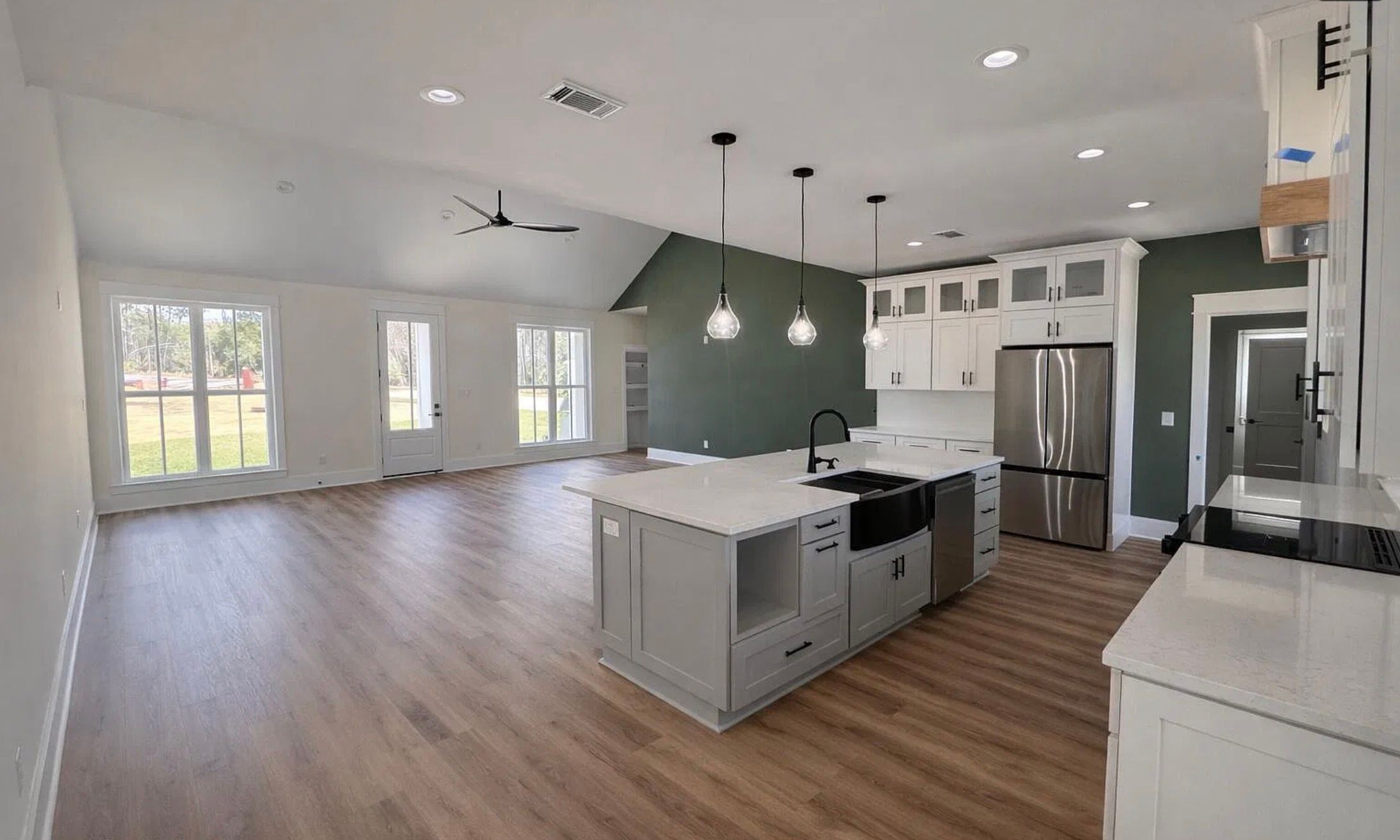 Kitchen with white cabinetry, an island, green wall, and adjoining living area.