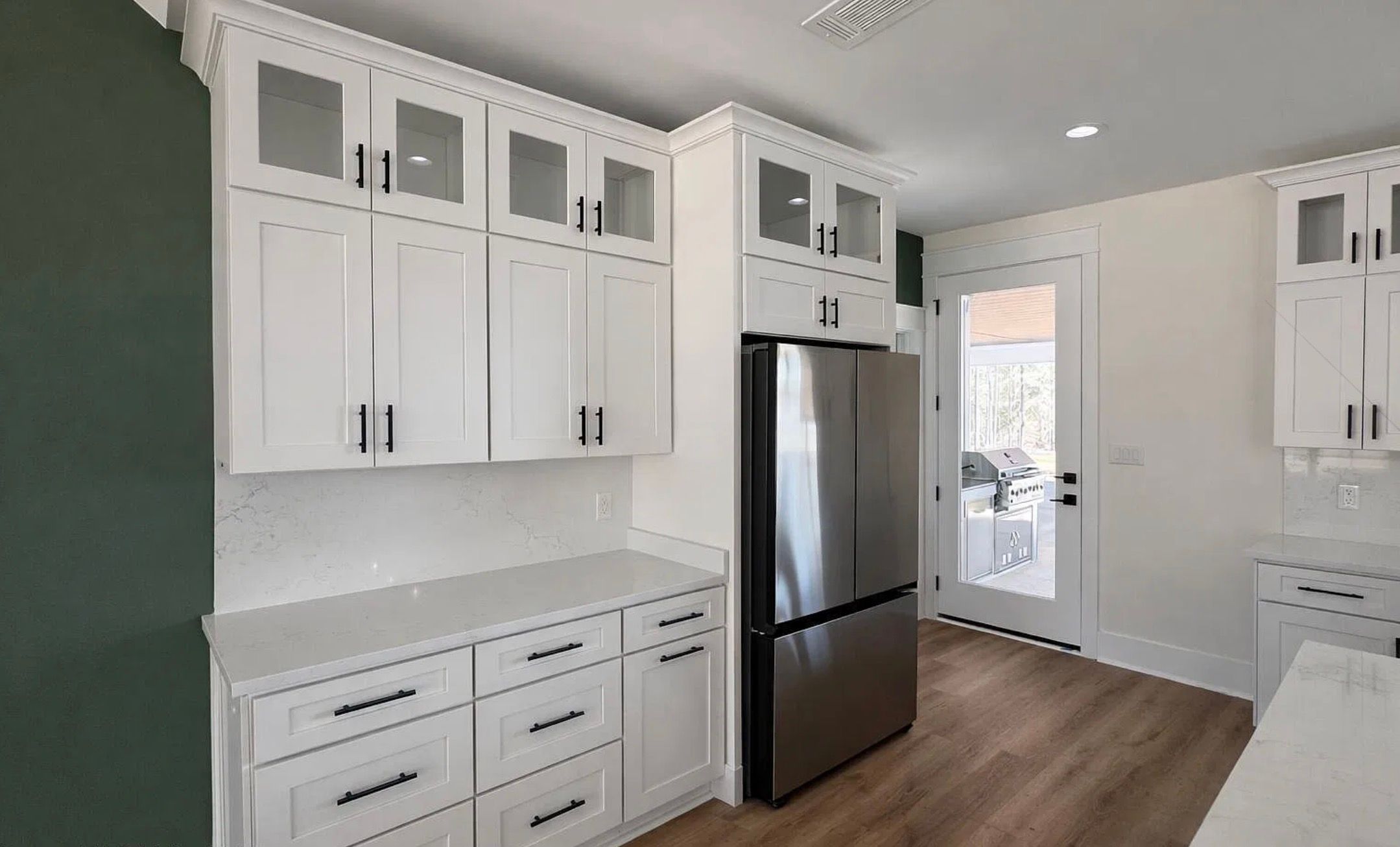 White kitchen cabinetry with black hardware, a stainless steel refrigerator, and green accent wall.