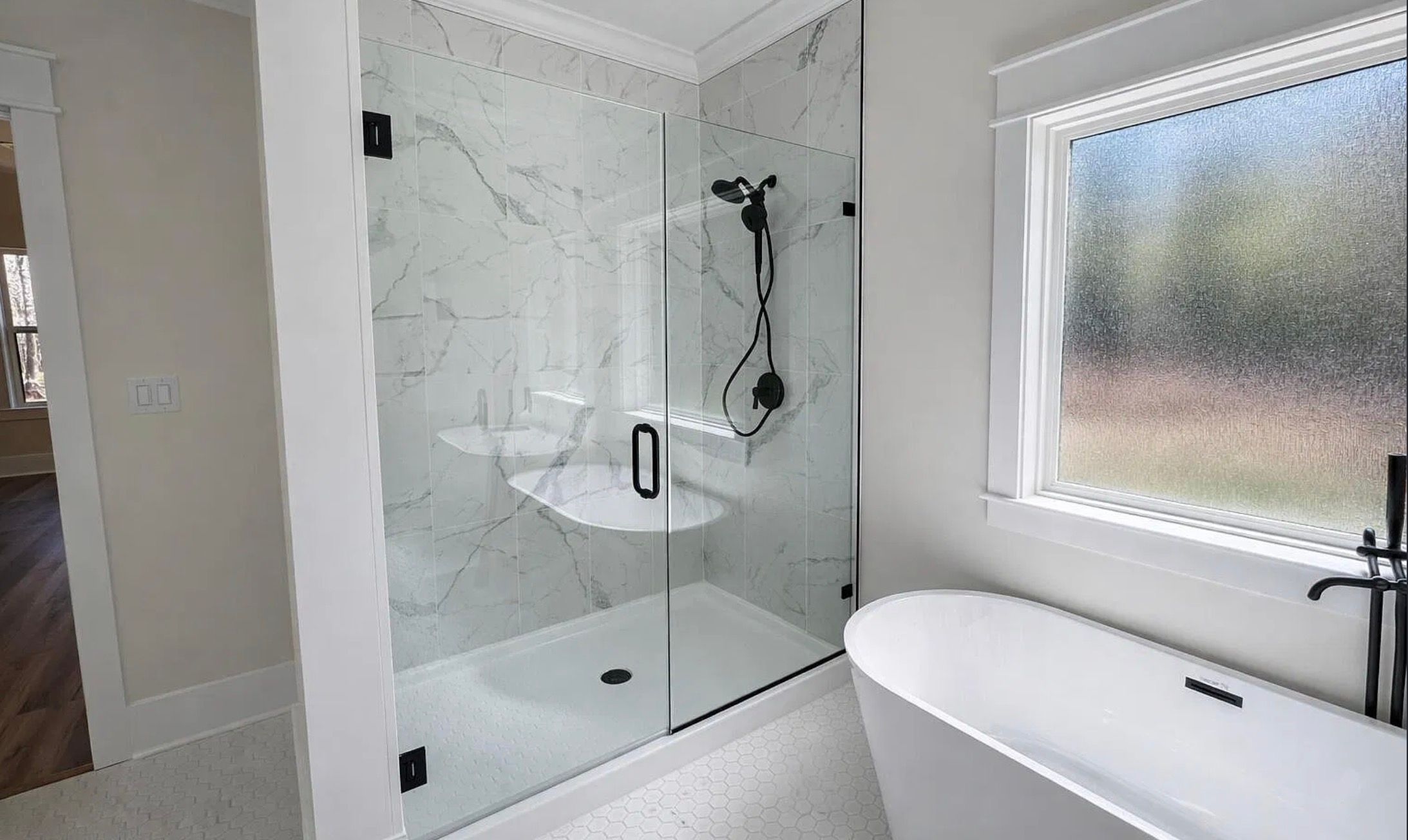 Bathroom with a glass shower, freestanding tub, marble-patterned surfaces, and black fixtures.