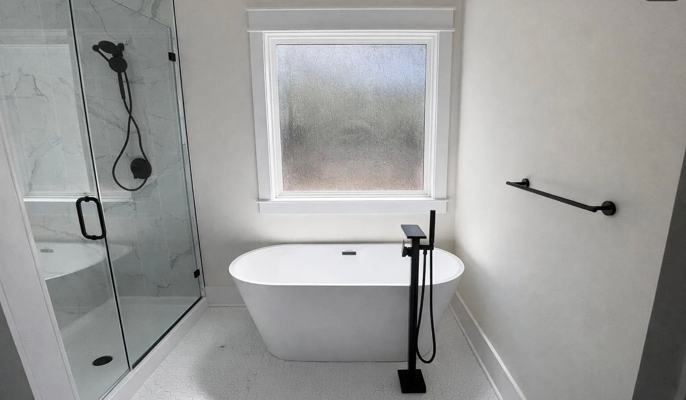 Freestanding white tub beside a glass shower and black fixtures beneath a frosted window.