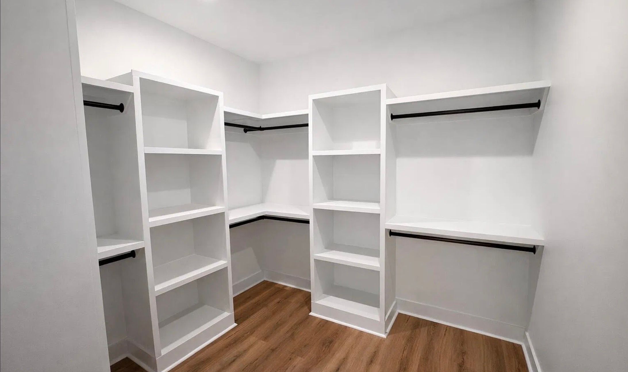 Walk-in closet with white built-in shelving, drawers, and black hanging rails.
