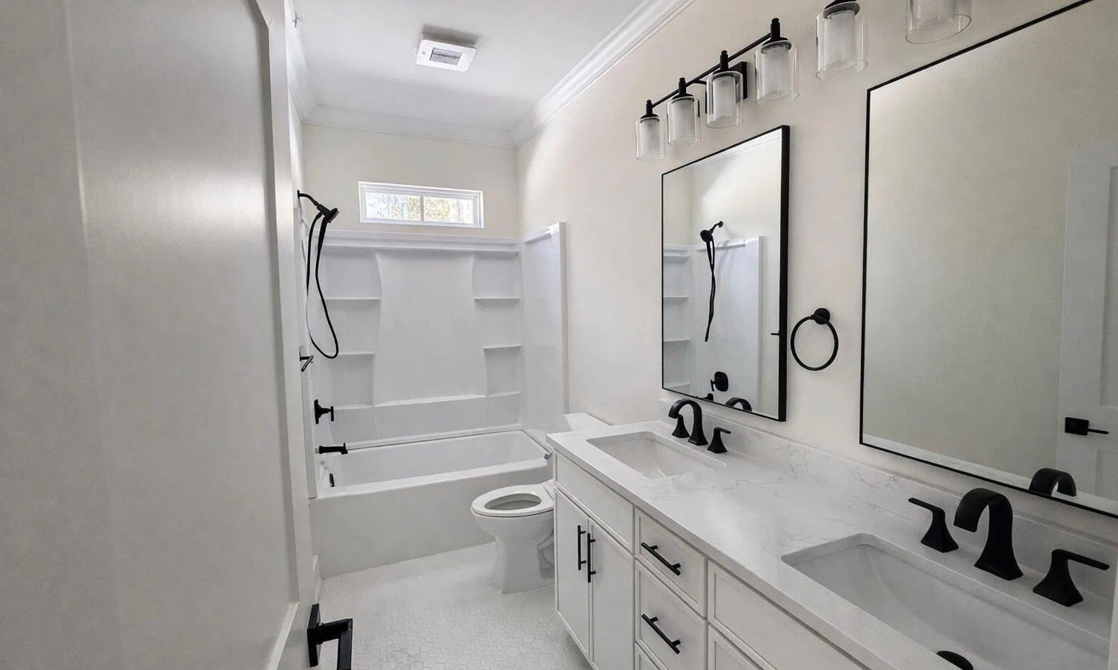 Bathroom vanity with two sinks, black fixtures, large mirrors, and white cabinetry.