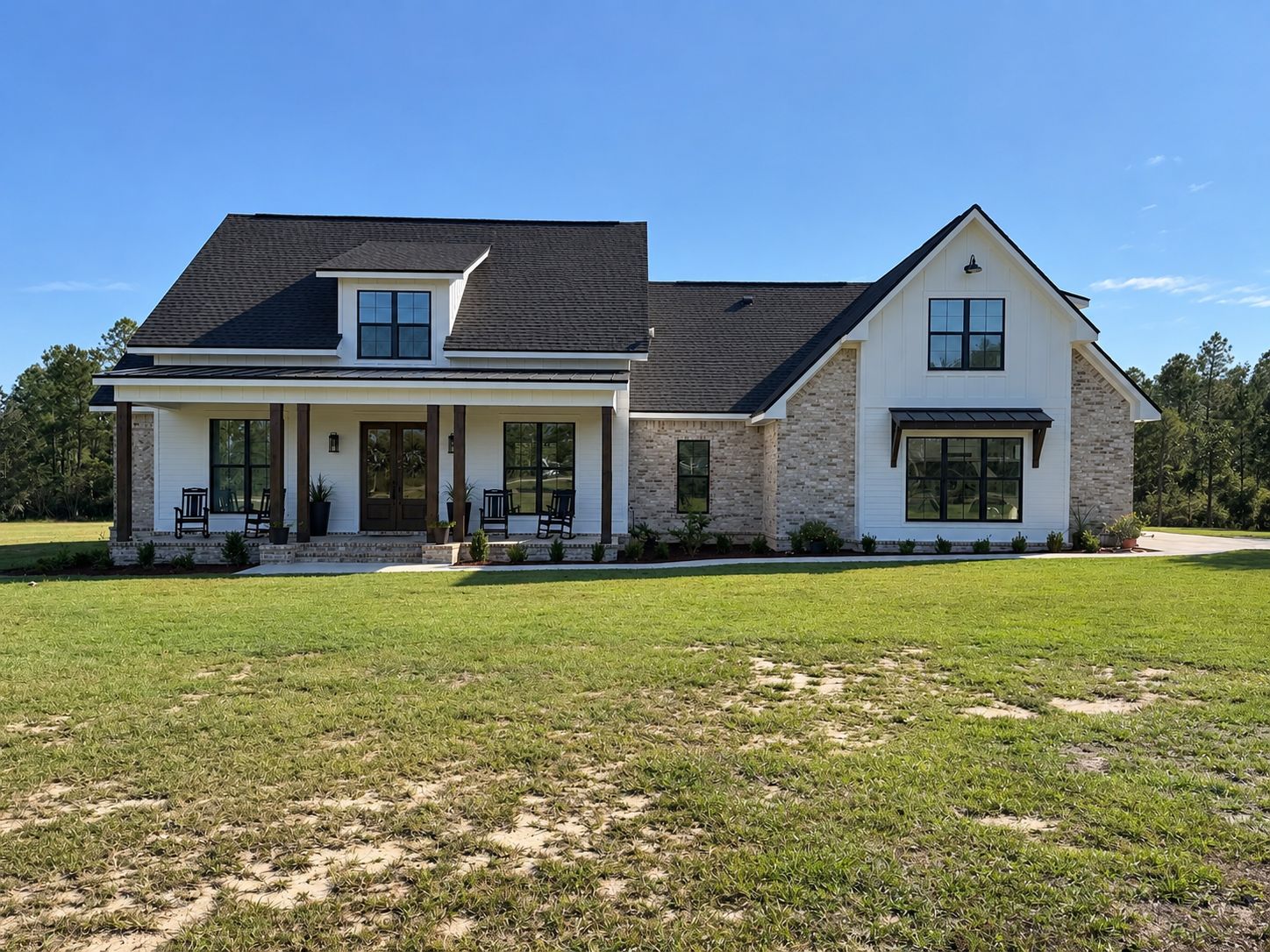 Front exterior of a completed light-brick and white home with a covered porch and dark roof.