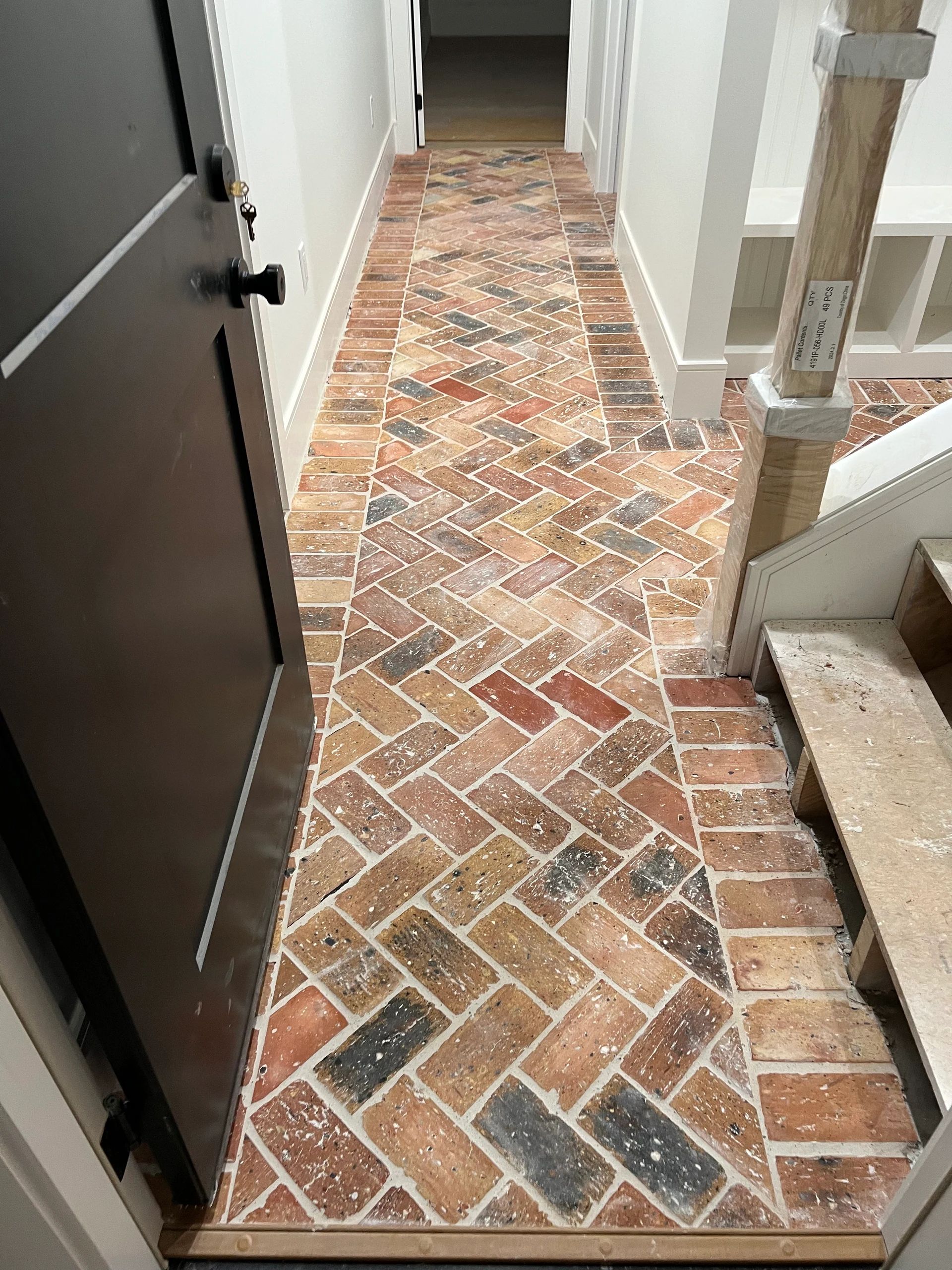 Entry hall with a black door, white built-in storage, staircase, and multicolor brick herringbone floor.