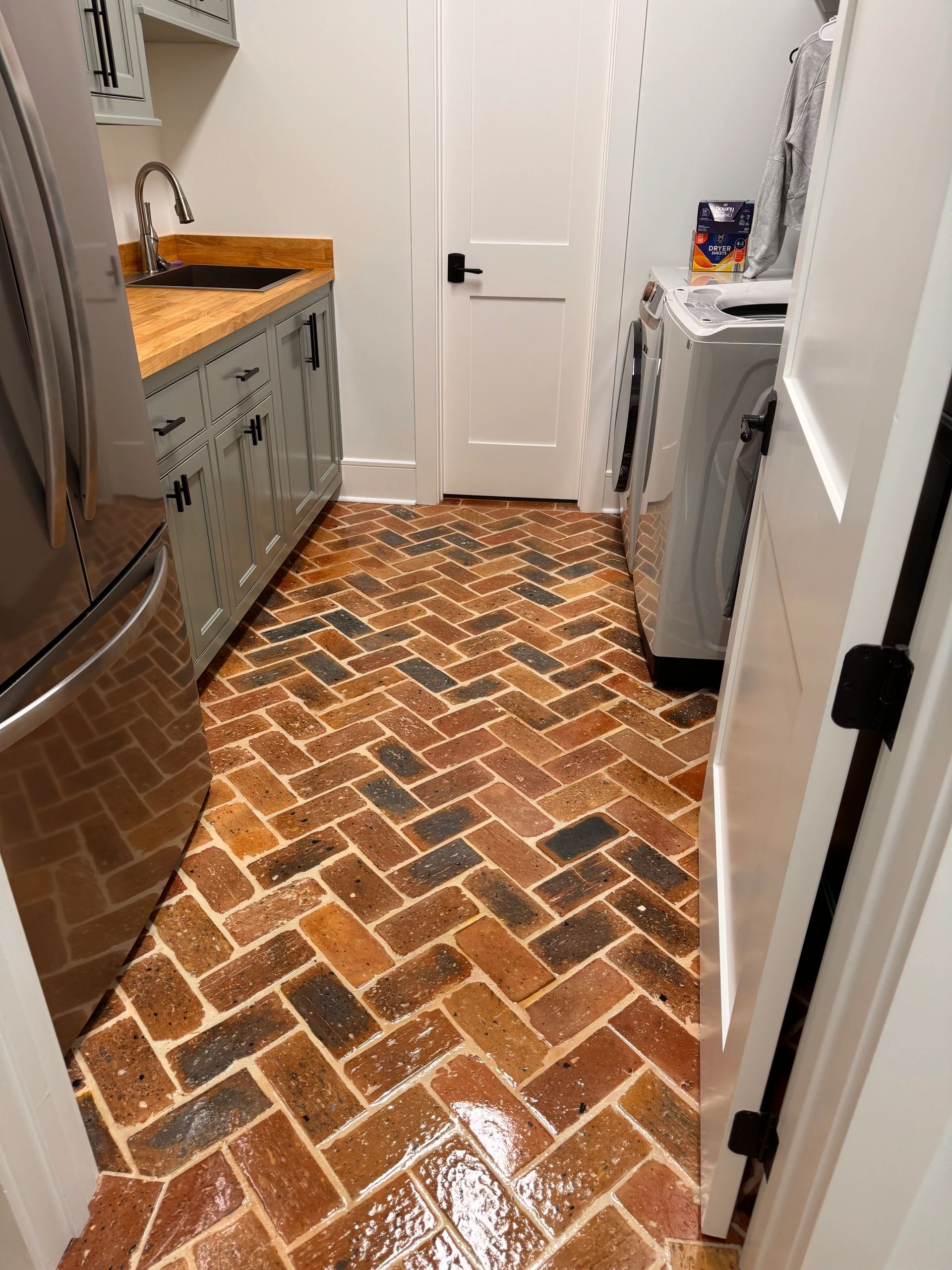 Laundry room with gray cabinets, a wood countertop, black sink, and multicolor brick herringbone floor.
