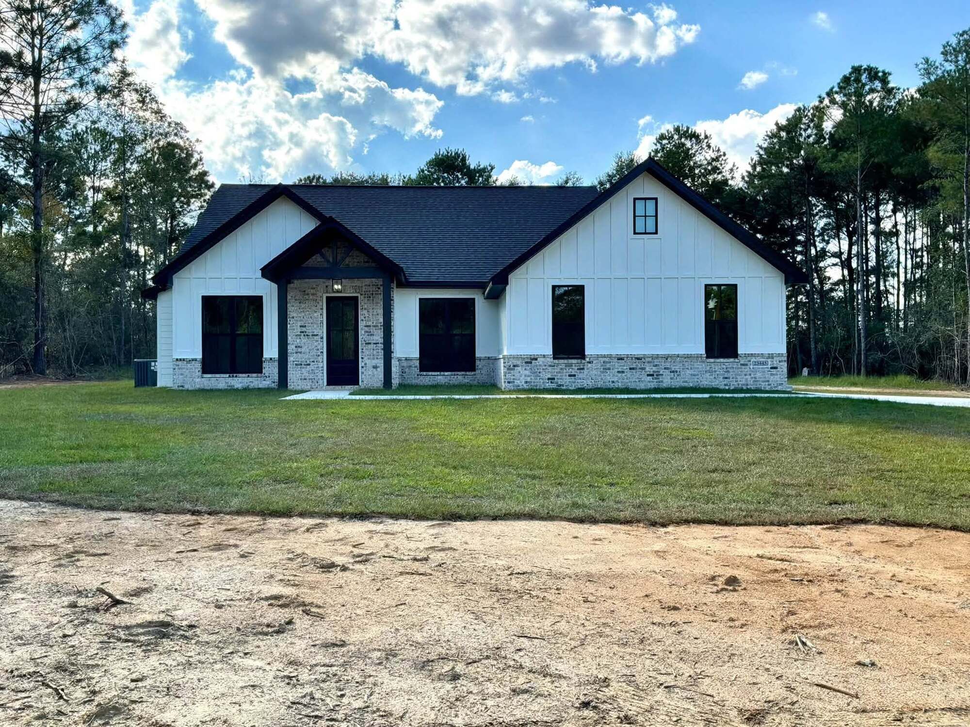 Completed Oasis Builders home with white siding, a dark roof, and a brick entry.